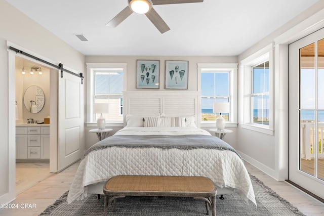 bedroom with ceiling fan, sink, a barn door, a water view, and light hardwood / wood-style flooring