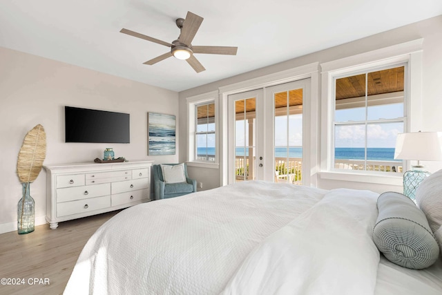 bedroom featuring access to outside, ceiling fan, a water view, light hardwood / wood-style flooring, and a beach view