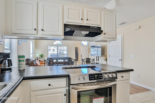 kitchen with a textured ceiling, light tile patterned floors, white cabinetry, and electric stove