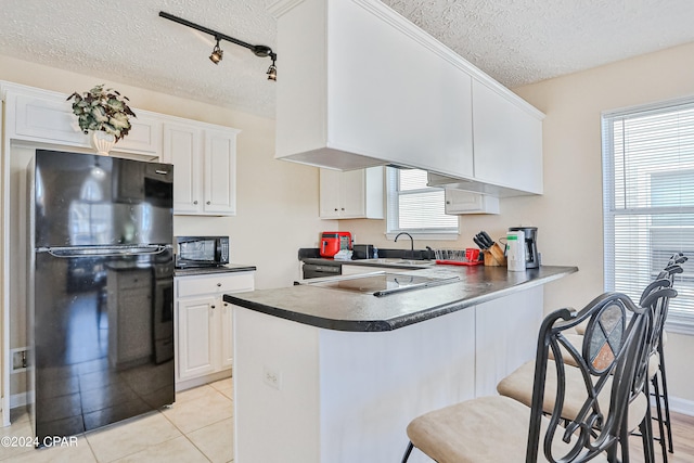 kitchen with a textured ceiling, white cabinets, black appliances, a kitchen breakfast bar, and kitchen peninsula