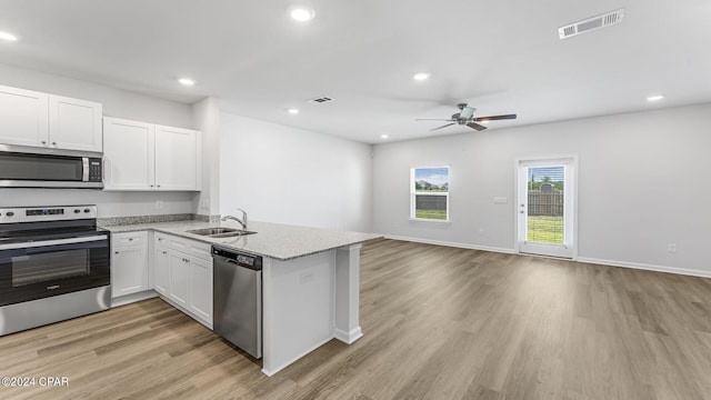 kitchen featuring stainless steel appliances, light stone countertops, white cabinets, sink, and kitchen peninsula