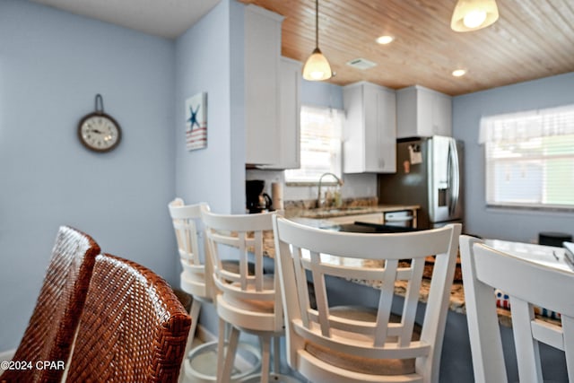 kitchen with white cabinets, wood ceiling, hanging light fixtures, sink, and stainless steel fridge with ice dispenser