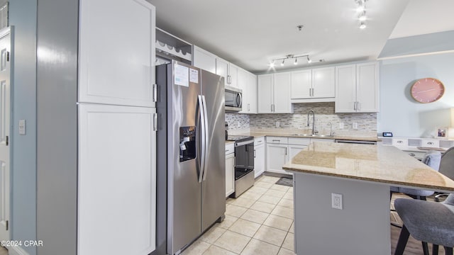 kitchen with appliances with stainless steel finishes, light stone counters, a kitchen island, sink, and white cabinetry