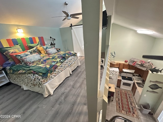 bedroom featuring hardwood / wood-style flooring, ceiling fan, a barn door, and vaulted ceiling