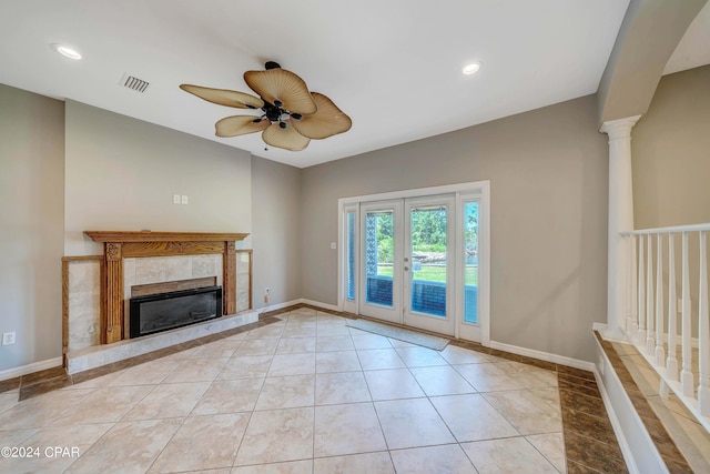 unfurnished living room with a tile fireplace, french doors, ceiling fan, ornate columns, and light tile patterned floors