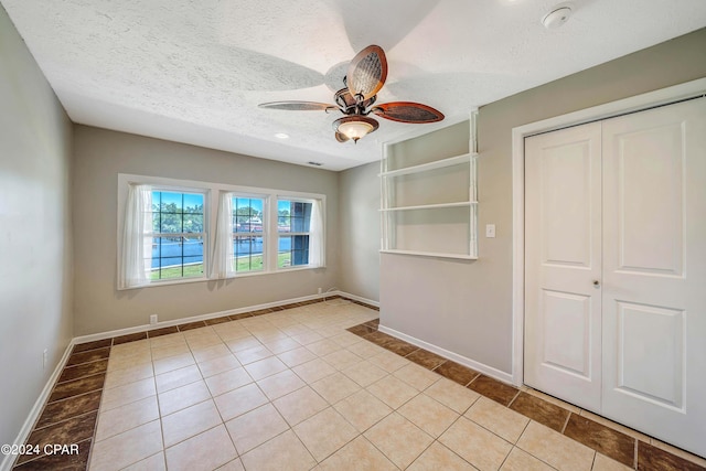 unfurnished bedroom with ceiling fan, a closet, light tile patterned floors, and a textured ceiling