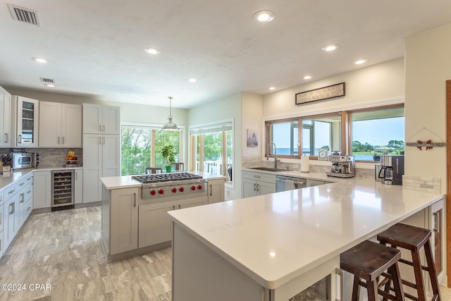 kitchen with appliances with stainless steel finishes, a breakfast bar, beverage cooler, sink, and pendant lighting