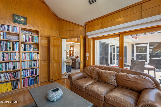 living room featuring built in shelves, wood walls, hardwood / wood-style floors, and vaulted ceiling