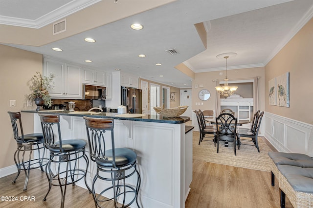 kitchen featuring dark countertops, visible vents, black appliances, crown molding, and a kitchen breakfast bar