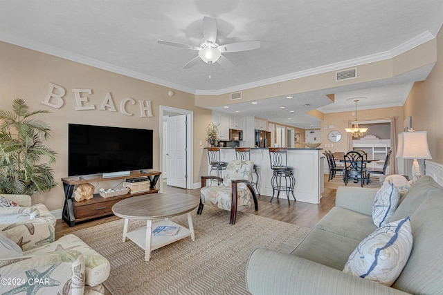 living area featuring visible vents, light wood-style floors, ornamental molding, and ceiling fan with notable chandelier