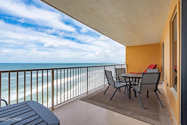 balcony with outdoor dining area, a water view, and a view of the beach