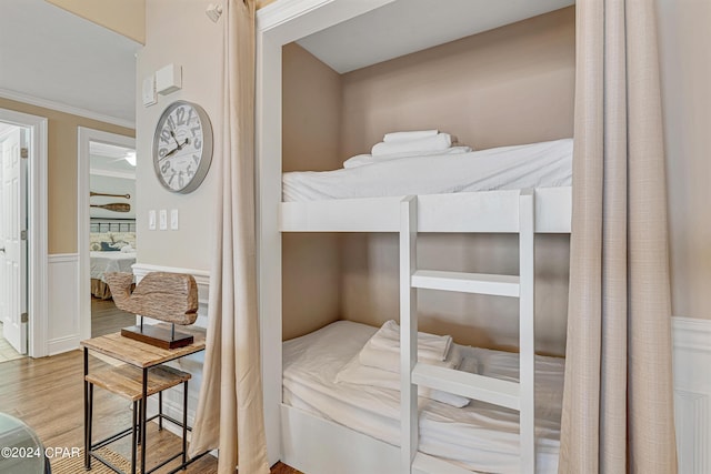 bedroom with wainscoting, ornamental molding, and wood finished floors