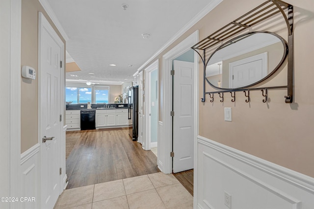 corridor featuring light tile patterned floors, wainscoting, crown molding, and a sink