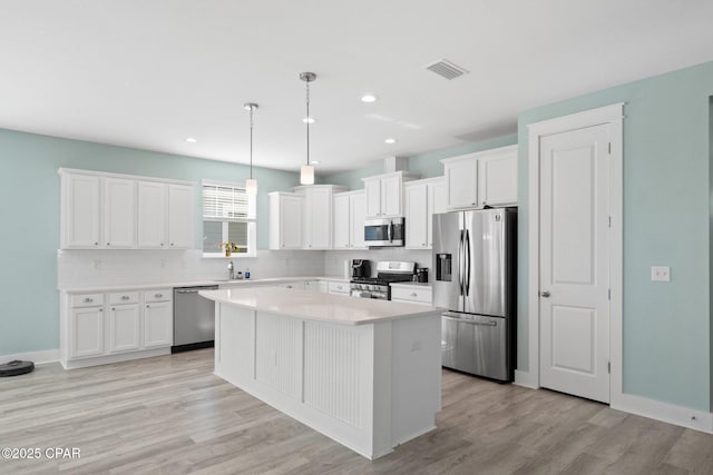 kitchen featuring appliances with stainless steel finishes, decorative light fixtures, light hardwood / wood-style flooring, white cabinets, and a kitchen island