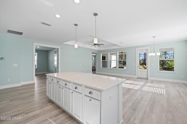 kitchen with white cabinets, ceiling fan with notable chandelier, a center island, and a healthy amount of sunlight