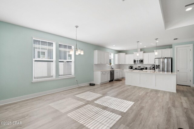 kitchen featuring a kitchen island, white cabinetry, stainless steel appliances, and hanging light fixtures