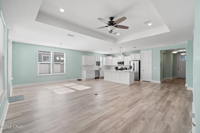 unfurnished living room featuring light hardwood / wood-style floors, a raised ceiling, and ceiling fan