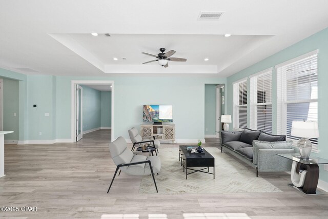 living room with light hardwood / wood-style flooring, a raised ceiling, and ceiling fan