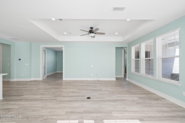 spare room with a raised ceiling, ceiling fan, and light hardwood / wood-style floors