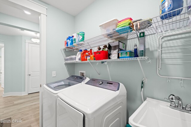 laundry area featuring washing machine and dryer, sink, and light hardwood / wood-style flooring