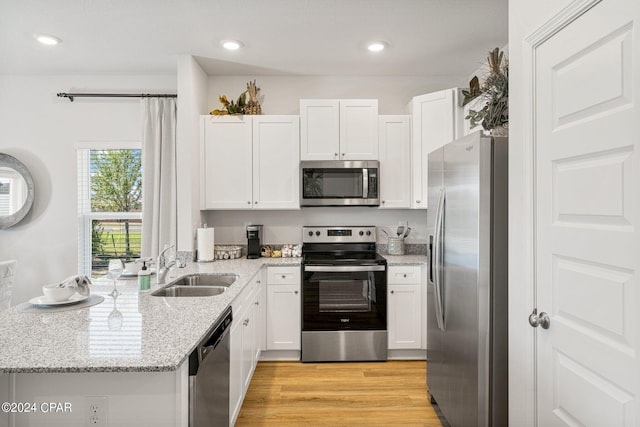 kitchen with light stone countertops, appliances with stainless steel finishes, sink, white cabinets, and light hardwood / wood-style floors