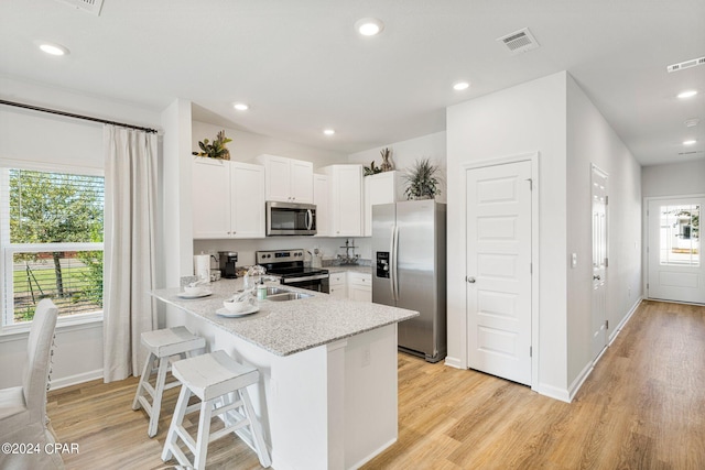 kitchen with light hardwood / wood-style floors, stainless steel appliances, kitchen peninsula, white cabinets, and a breakfast bar area