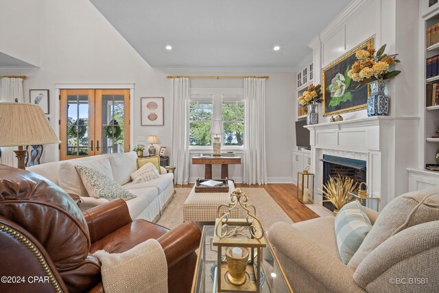 living room featuring french doors, ornamental molding, built in shelves, and light wood-type flooring