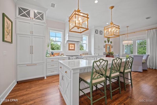 kitchen featuring ornamental molding, an island with sink, white cabinets, a kitchen bar, and decorative light fixtures