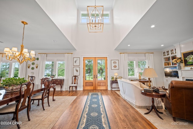 foyer featuring french doors, crown molding, light wood-type flooring, and a notable chandelier