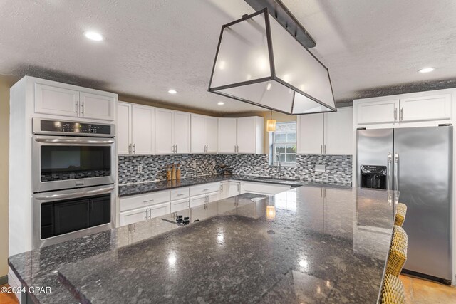 kitchen with decorative light fixtures, stainless steel appliances, dark stone counters, and white cabinets