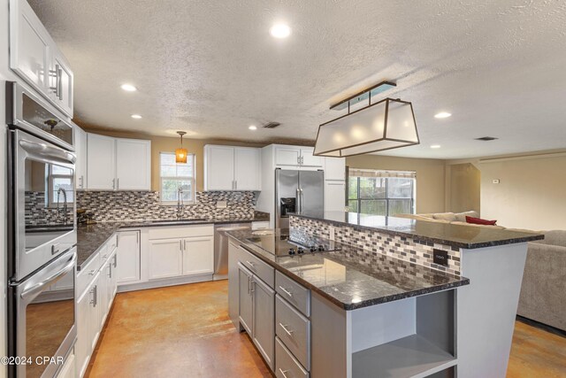 kitchen with stainless steel appliances, white cabinets, a center island, and decorative light fixtures