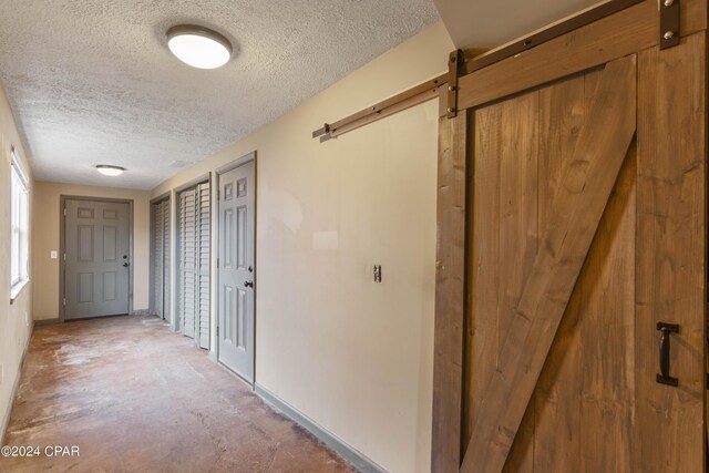 hallway featuring a barn door, concrete floors, and a textured ceiling