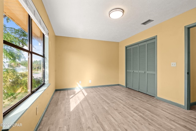 unfurnished bedroom featuring a textured ceiling, a closet, and light hardwood / wood-style flooring