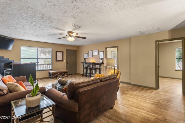 living room featuring light hardwood / wood-style floors, a textured ceiling, ceiling fan, and a healthy amount of sunlight