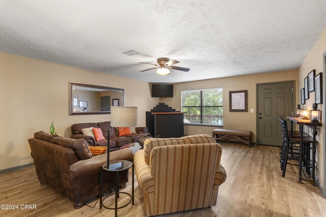 living room featuring ceiling fan, light hardwood / wood-style flooring, and a textured ceiling