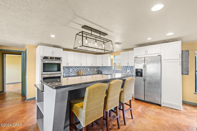 kitchen with white cabinetry, stainless steel appliances, a center island, decorative light fixtures, and backsplash