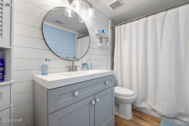 bathroom featuring wood-type flooring, vanity, toilet, and wooden walls