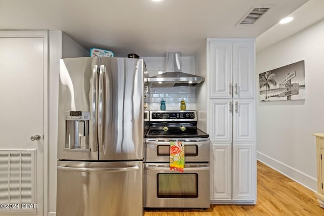 kitchen featuring wall chimney exhaust hood, backsplash, appliances with stainless steel finishes, white cabinets, and light wood-type flooring