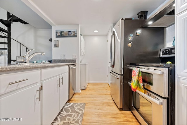 kitchen with appliances with stainless steel finishes, light wood-type flooring, sink, wall chimney range hood, and white cabinets