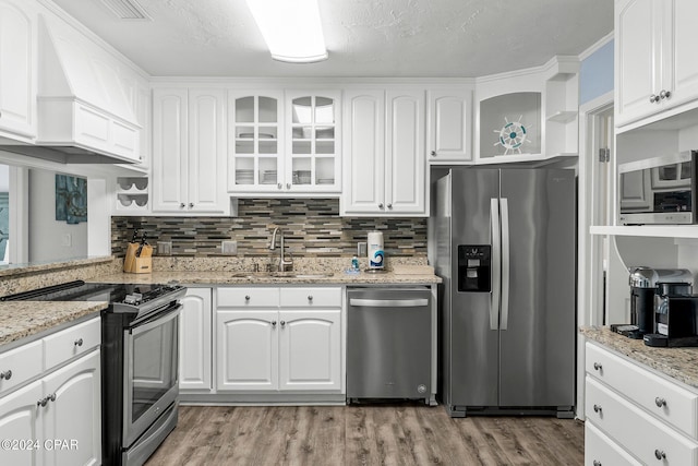 kitchen featuring stainless steel appliances, a sink, white cabinets, light wood finished floors, and glass insert cabinets