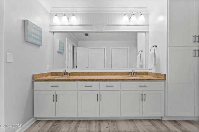 full bath with double vanity, wood finished floors, a sink, and crown molding