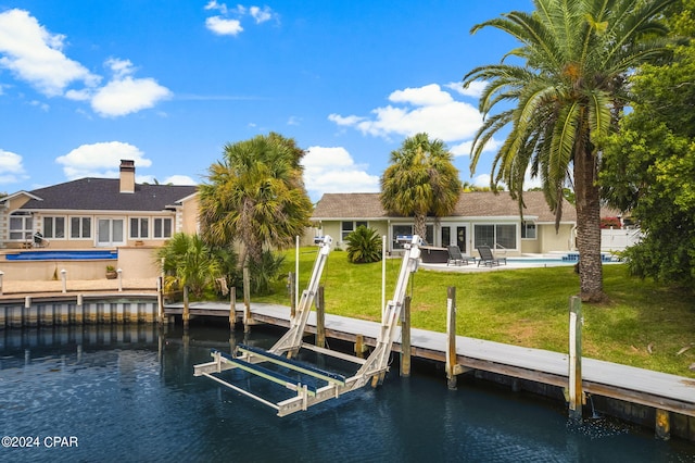 dock area with an outdoor pool, a water view, a yard, and boat lift