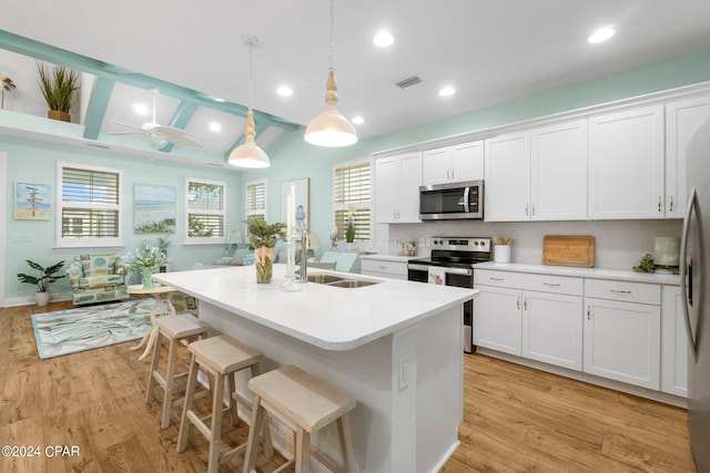 kitchen with hanging light fixtures, stainless steel appliances, a breakfast bar, a kitchen island with sink, and white cabinets