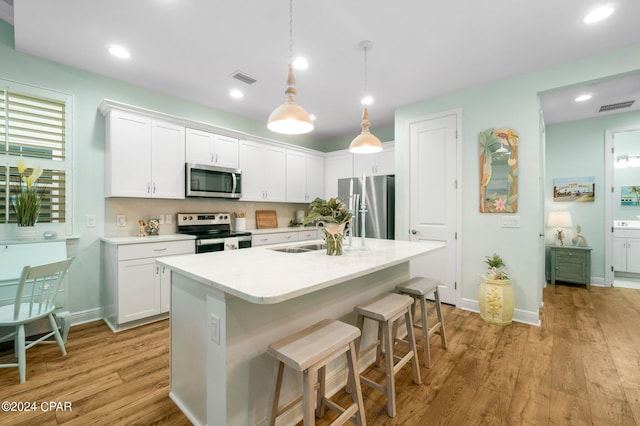 kitchen featuring decorative light fixtures, sink, white cabinetry, a kitchen island with sink, and stainless steel appliances