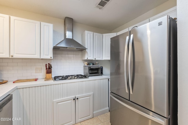 kitchen featuring white cabinets, light tile patterned floors, wall chimney range hood, and appliances with stainless steel finishes