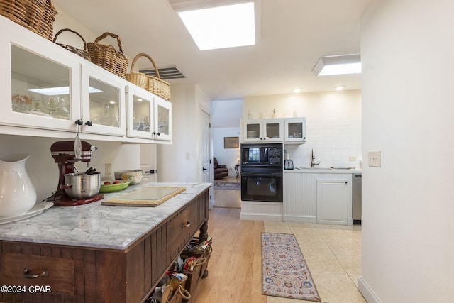 kitchen with light wood-type flooring, tasteful backsplash, dark brown cabinets, black appliances, and white cabinets