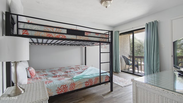 bedroom featuring access to exterior, a textured ceiling, and wood finished floors