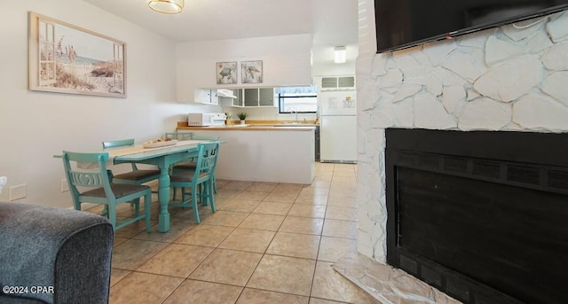 kitchen with light tile patterned floors, a peninsula, a fireplace, exhaust hood, and freestanding refrigerator