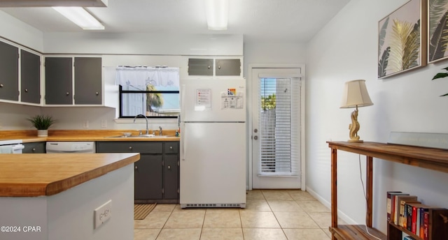 kitchen with a sink, wood counters, light tile patterned floors, white appliances, and baseboards