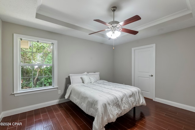 bedroom featuring a tray ceiling, dark wood-type flooring, and ceiling fan